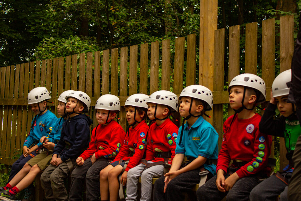 Squirrels and Beavers, wearing climbing helmets, waiting on a bench.